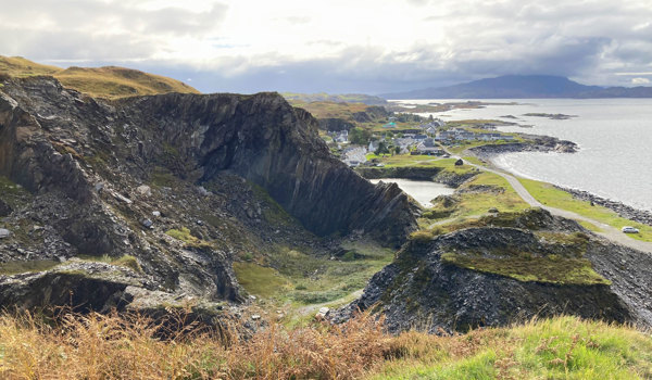 View out over a slate quarry on isle of Luing. Shows quarry, with town and sea behind. 