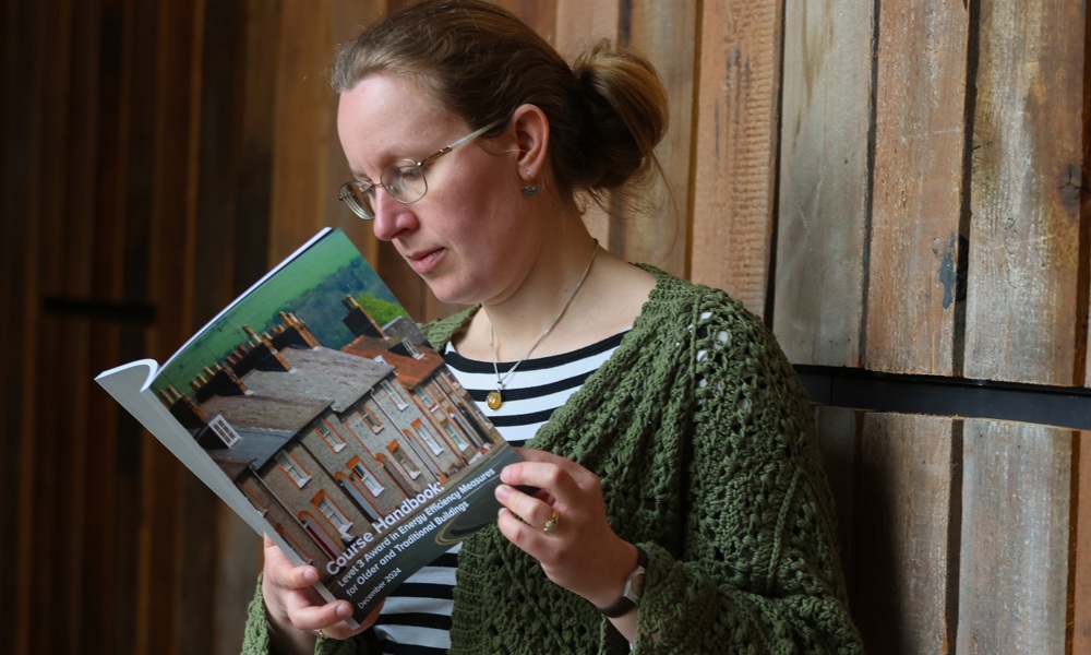 A learner reading a printed version of the course handbook. The title page includes a picture of a row of traditional houses.