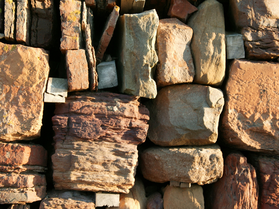 A drystane wall of reddish stone is held in place with wooden chocks.