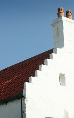 A white lime washed house with a crow stepped roof with red pantiles.