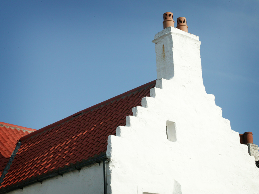 A house where 'steps' form the gable end of the roof going up to the chimney. The house is coated with white lime wash and has a pantile roof