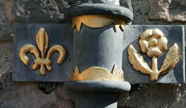 Black downpipe decorated with gold coloured fleur-de-lis and rose emblems to its sides