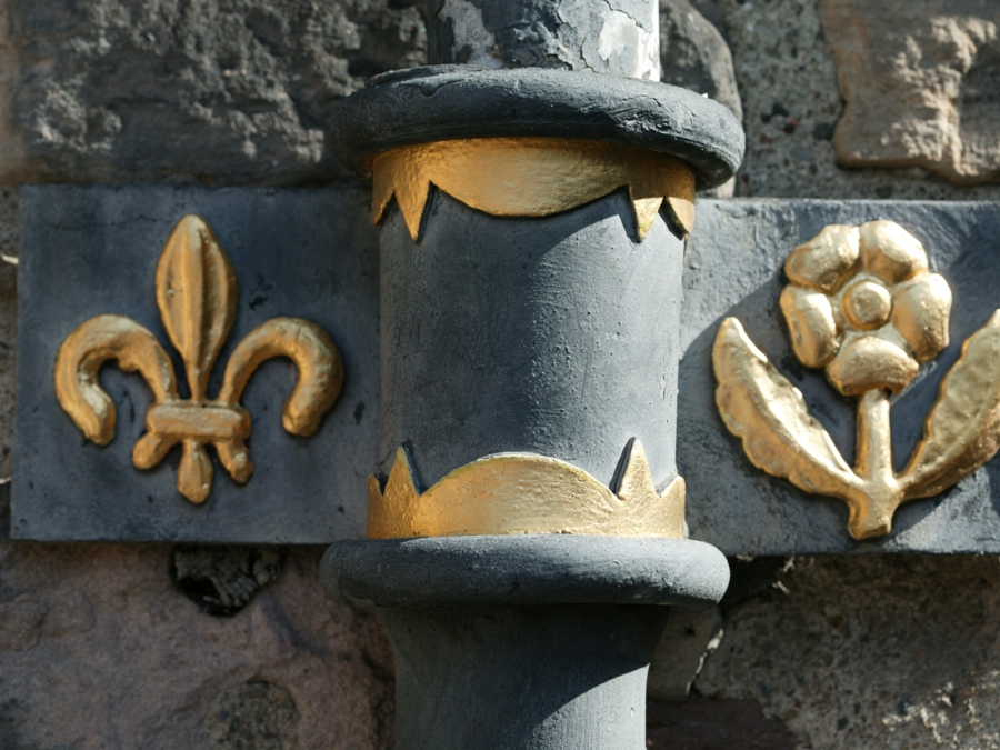 Black downpipe decorated with gold coloured fleur-de-lis and rose emblems to its sides