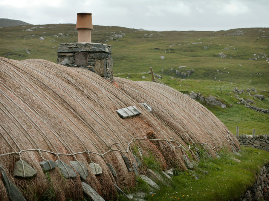 Wide view of house with ropes with heavy stones at the ends holding down thatched roof