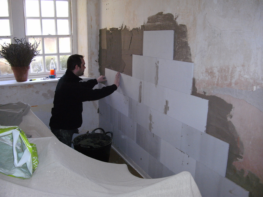 A person installing insulation board to the inside wall of a house