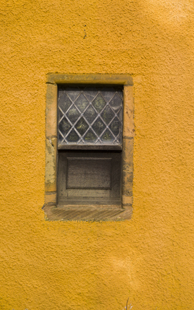 A yellow, lime-wahed building with a leaded window.