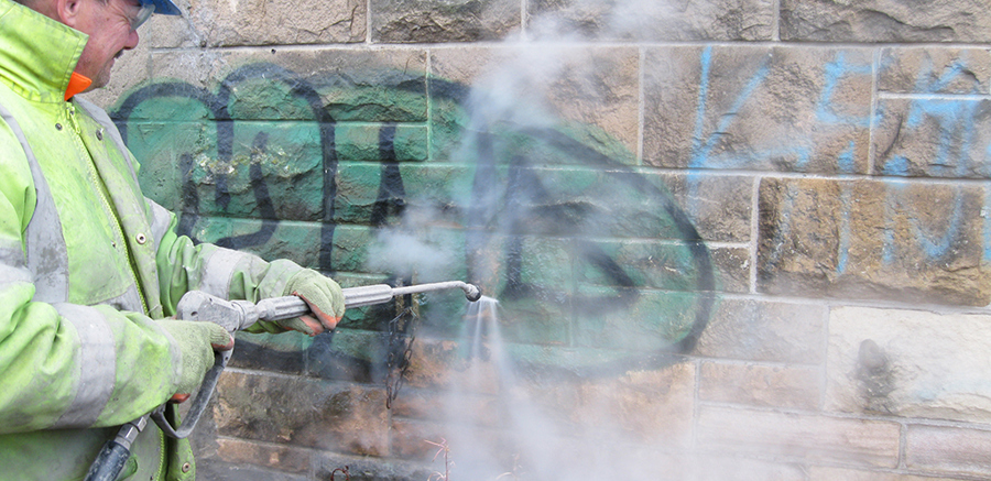 Water blasting graffiti removal on a stone wall