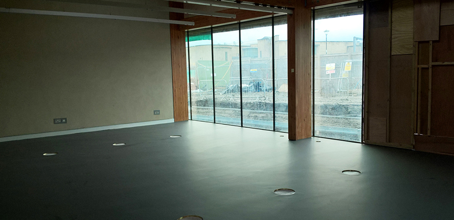 A large, empty room with tall, floor to ceiling windows.