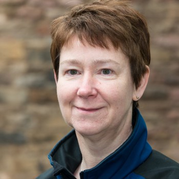 A person with short hair, wearing a high-neck blue fleece, smiling