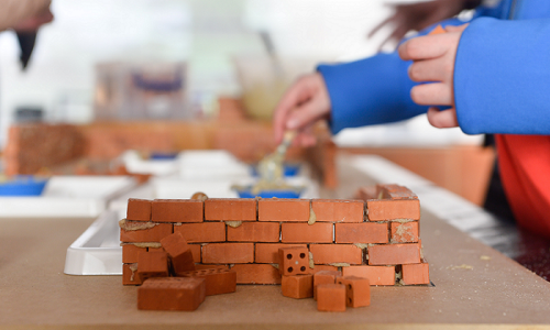 A child building a wall from min bricks and mortar on a table