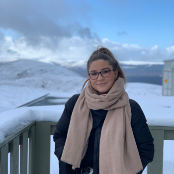 Abi smiling, outside in the snow, wearing a pink scarf and black coat