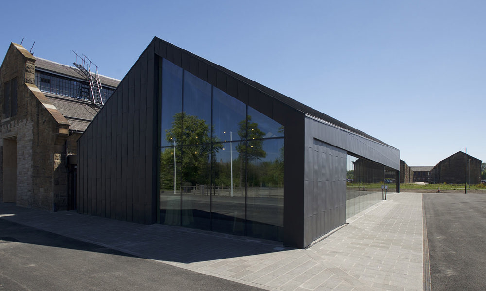 A side view of the Engine Shed, which has a traditional stone building in the middle, flanked by two black and glass modern wings.