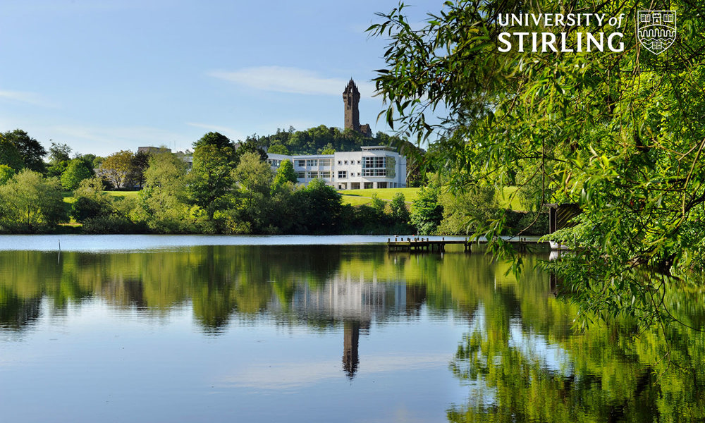 A photo of Stirling University behind a beautiful loch and trees
