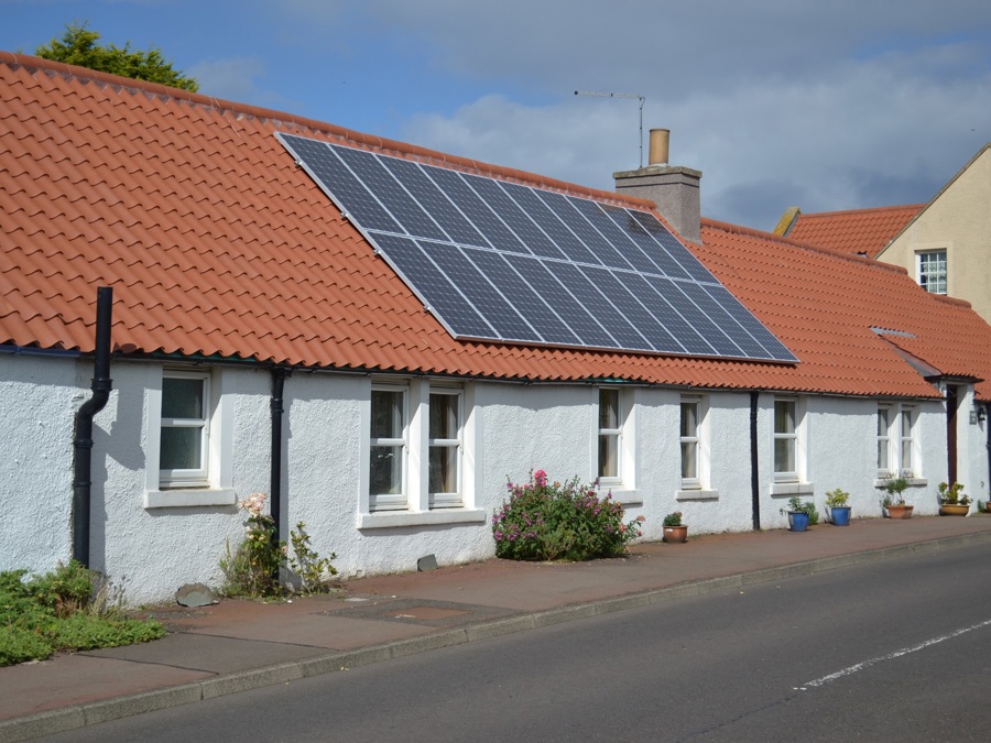 A traditional row of cottage bungalows with an orange pantile roof fitted with solar panels