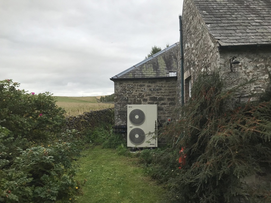 An air source heat pump unit attached to the side of a traditional stone building