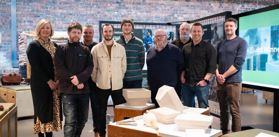 Nine members of staff stand behind a display of stonemasonry work, with exhibition panels behind. 