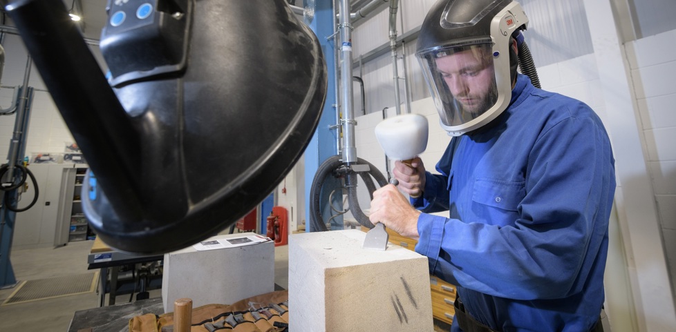 A person using hand tools to carve into a block of stone in a workshop