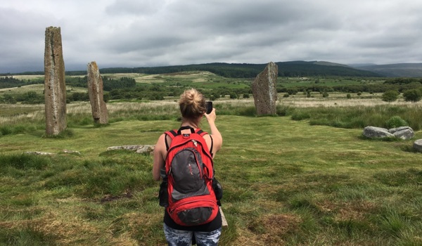 A person taking a photo of a group of tall, historic standing stones