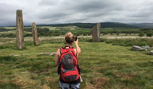 A person taking a photo of a group of tall, historic standing stones