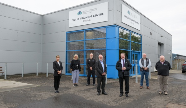 A number of people are standing in front of a large building with blue doors. The logo at the top says Historic Environment Scotland Skills Training Center Stirling.