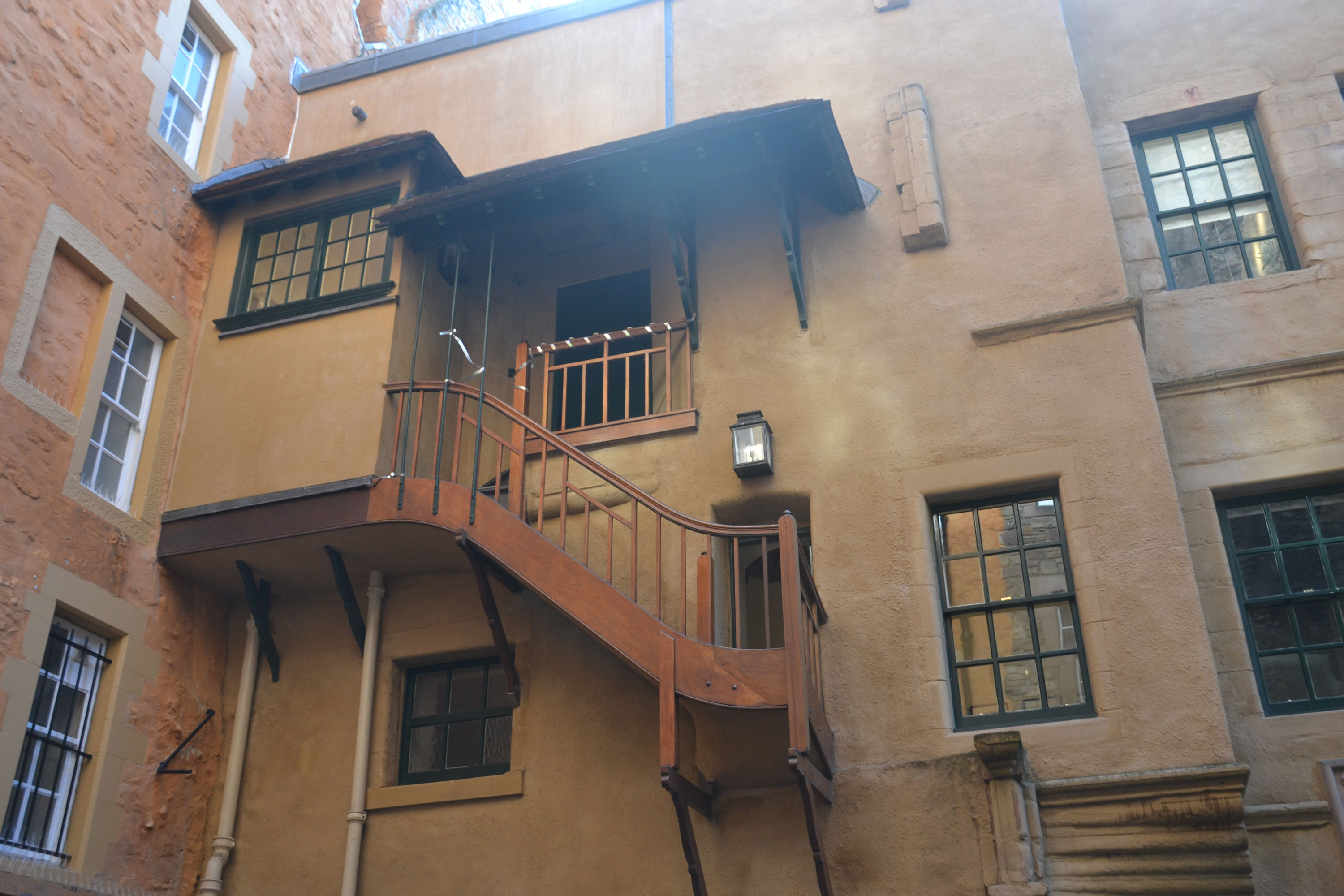 A view looking up at a traditional building that has a yellow lime render, traditional wooden windows and an exterior wooden stair. 