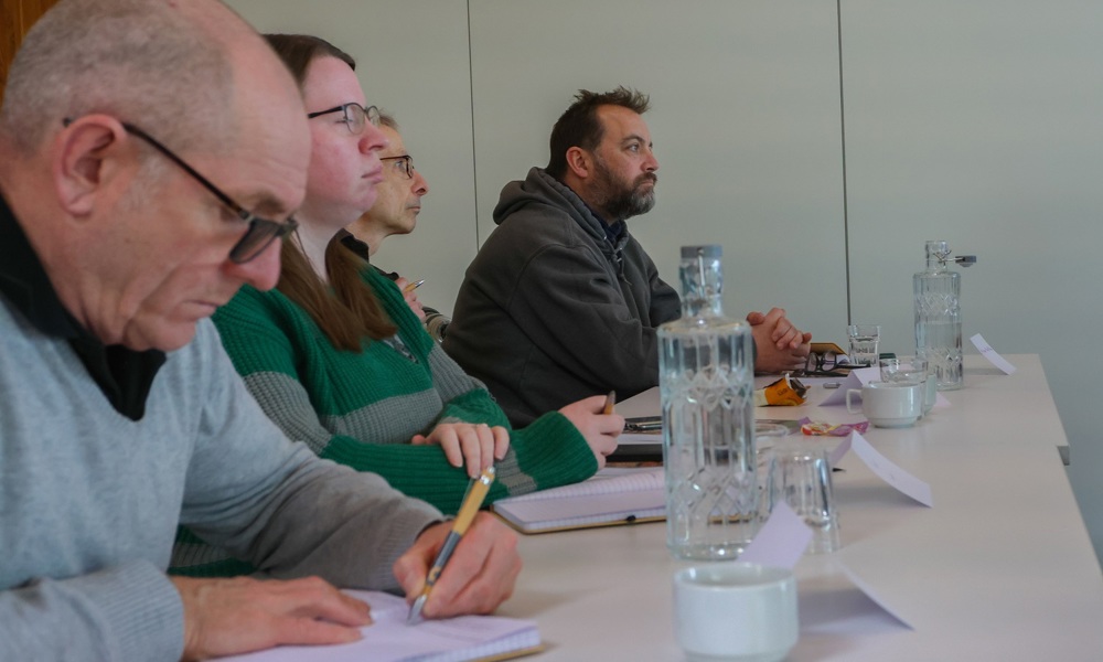 Four learners sitting at a table, taking notes and listening. 