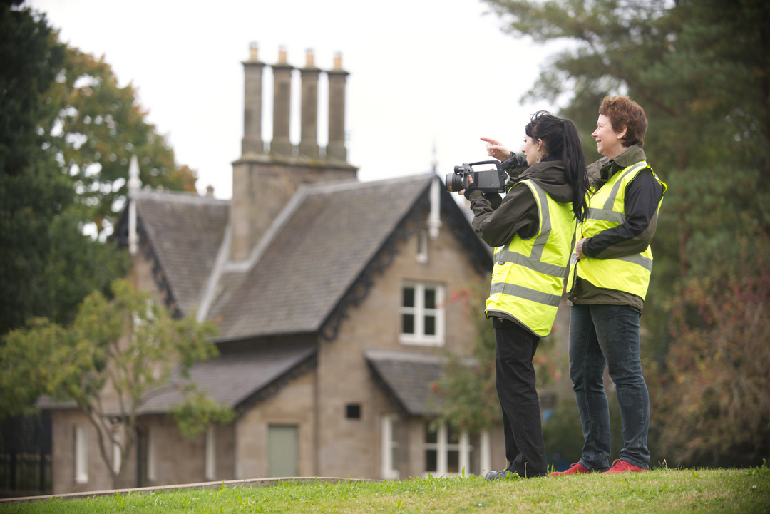 Two HES staff members wearing high-visibility yellow vests. They are standing in front of a traditional building, with equipment to survey it.