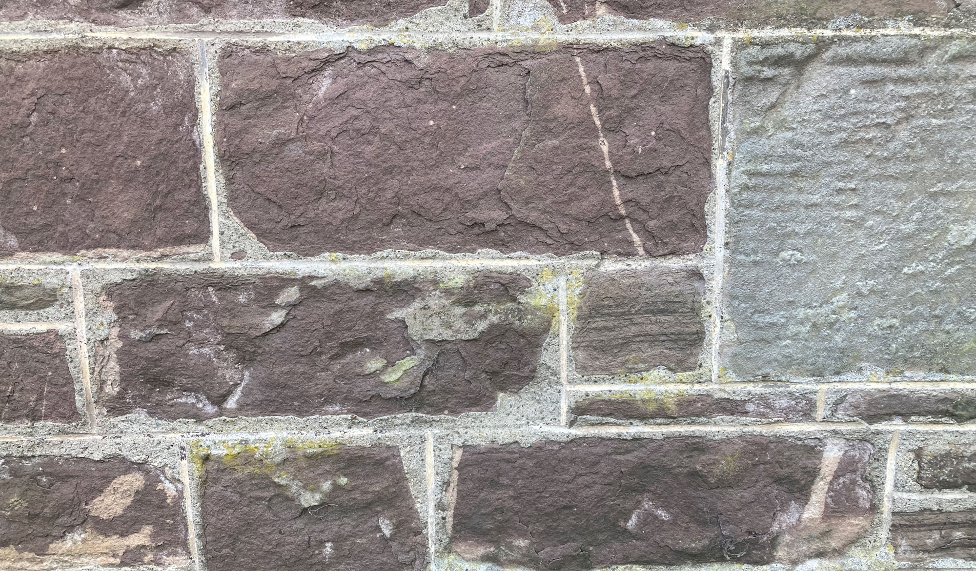 A section of a stone wall that has light lime mortar lines between the stones.