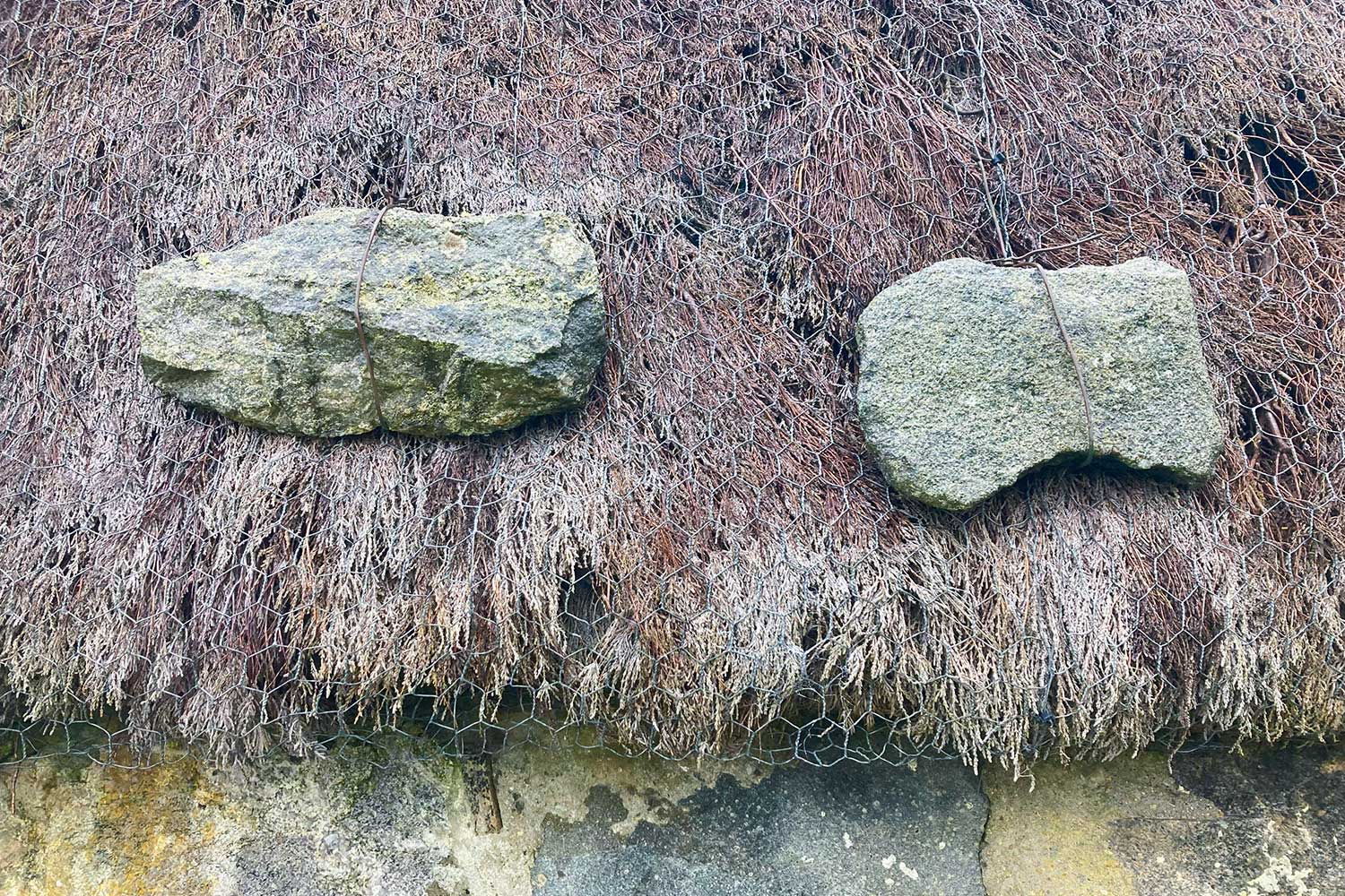 A thatch roof, with large stones tied to hold it down at the edges. 