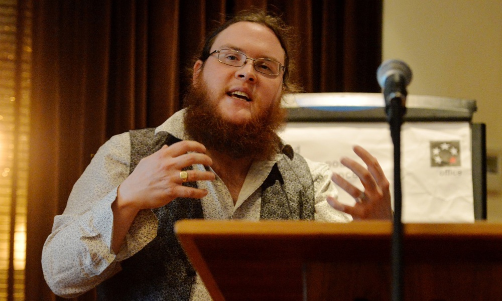 A portrait of Moses Jenkins, while he is giving an animated talk behind a lectern.