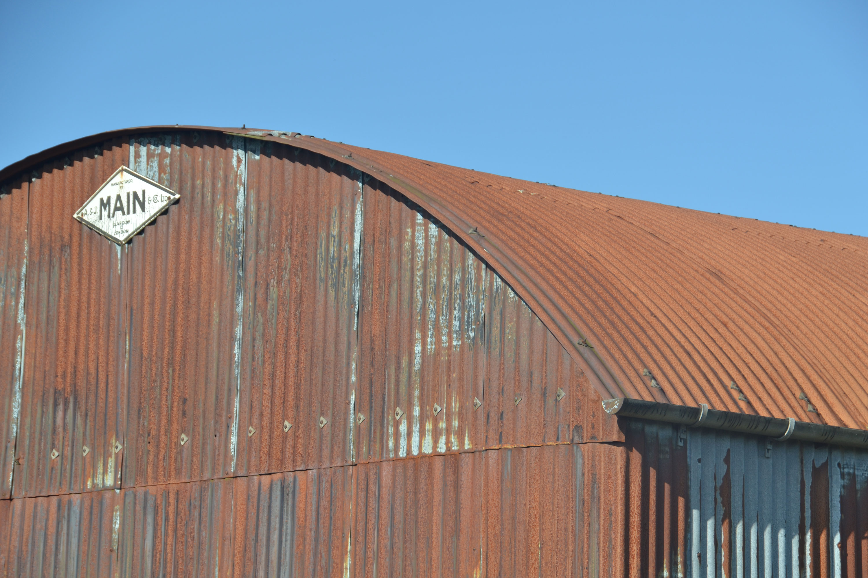 A large industrial shed coated in iron corrugated sheeting. The roof as a big curve to it and the iron sheeting has turned a brownish red colour. 