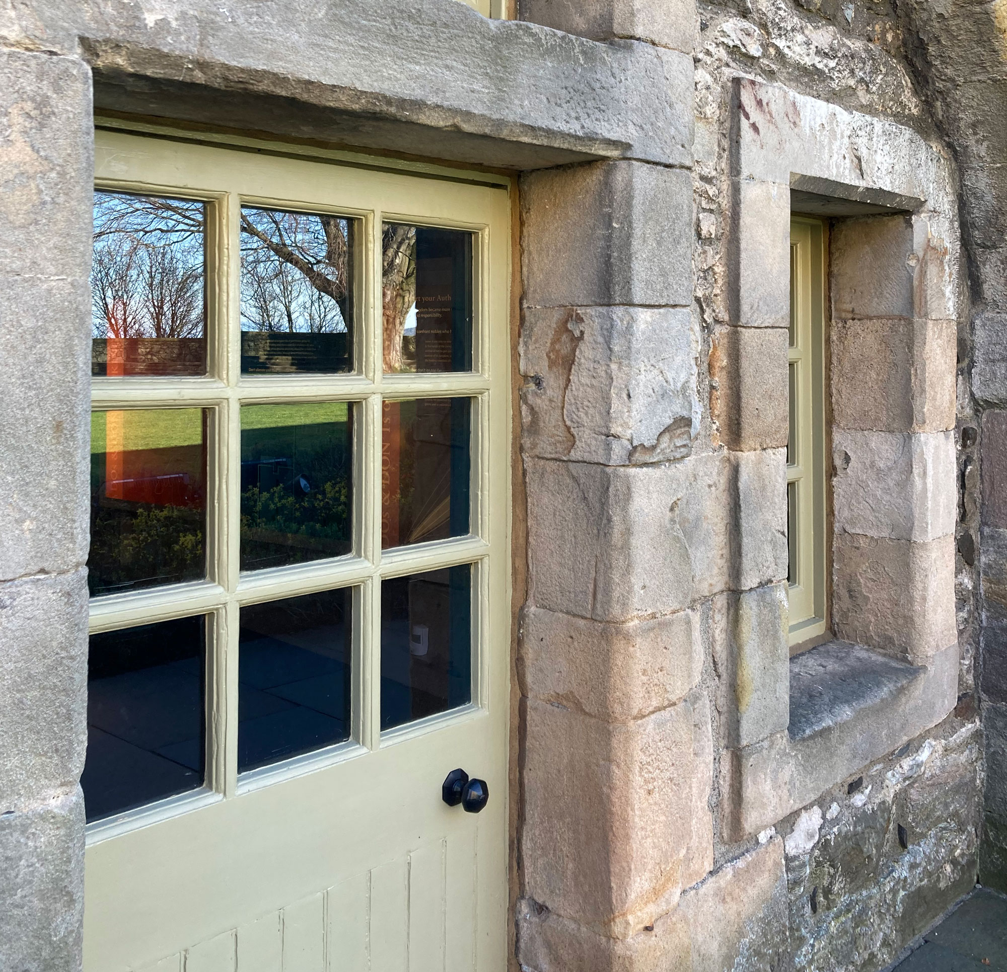 An exterior view of a traditional stone building. A wooden door, with 9 small glass panels is the primary focus.