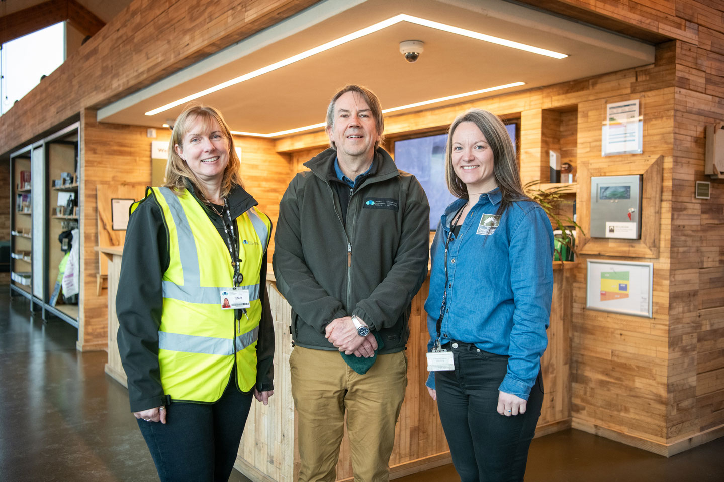Three members of staff. The first on left is wearing a high-vis vest and lanyard, the next is wearing a branded green fleece and the third is wearing a branded denimn shirt. 