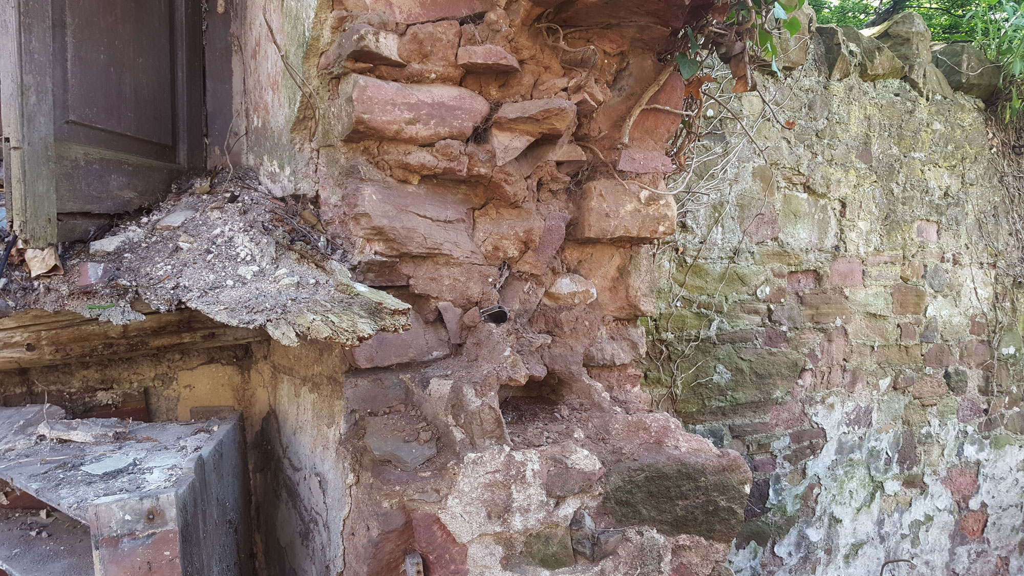 A section of a wall of a building. the corner has crumbled revealing earth mortar on the interior.